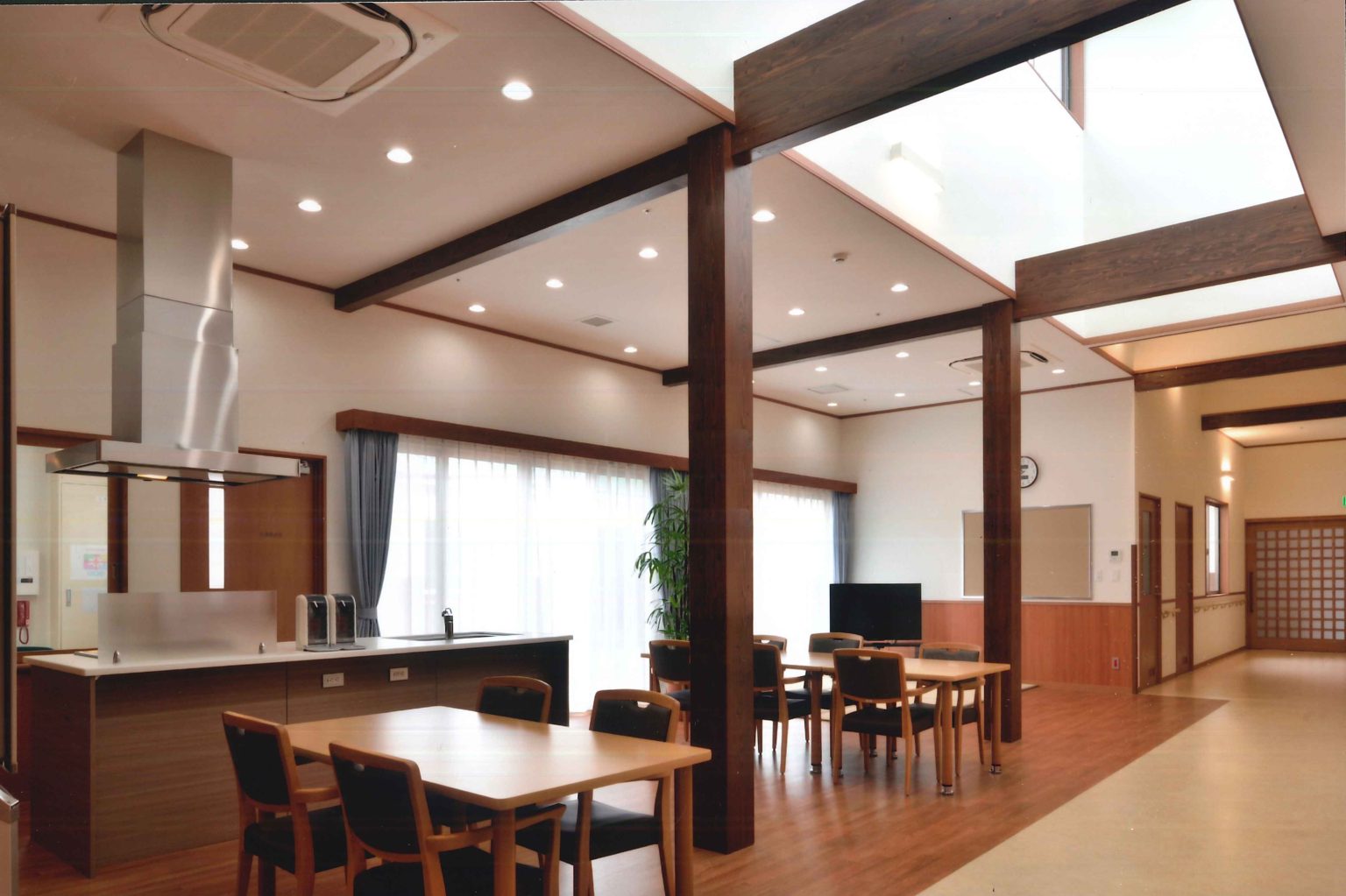 木梁の開放的なリビング・ダイニング空間。キッチン、食卓、テレビエリアが一体配置。